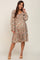 Smiling woman wearing a long sleeve floral smocked maternity dress with tiered skirt and tan heels