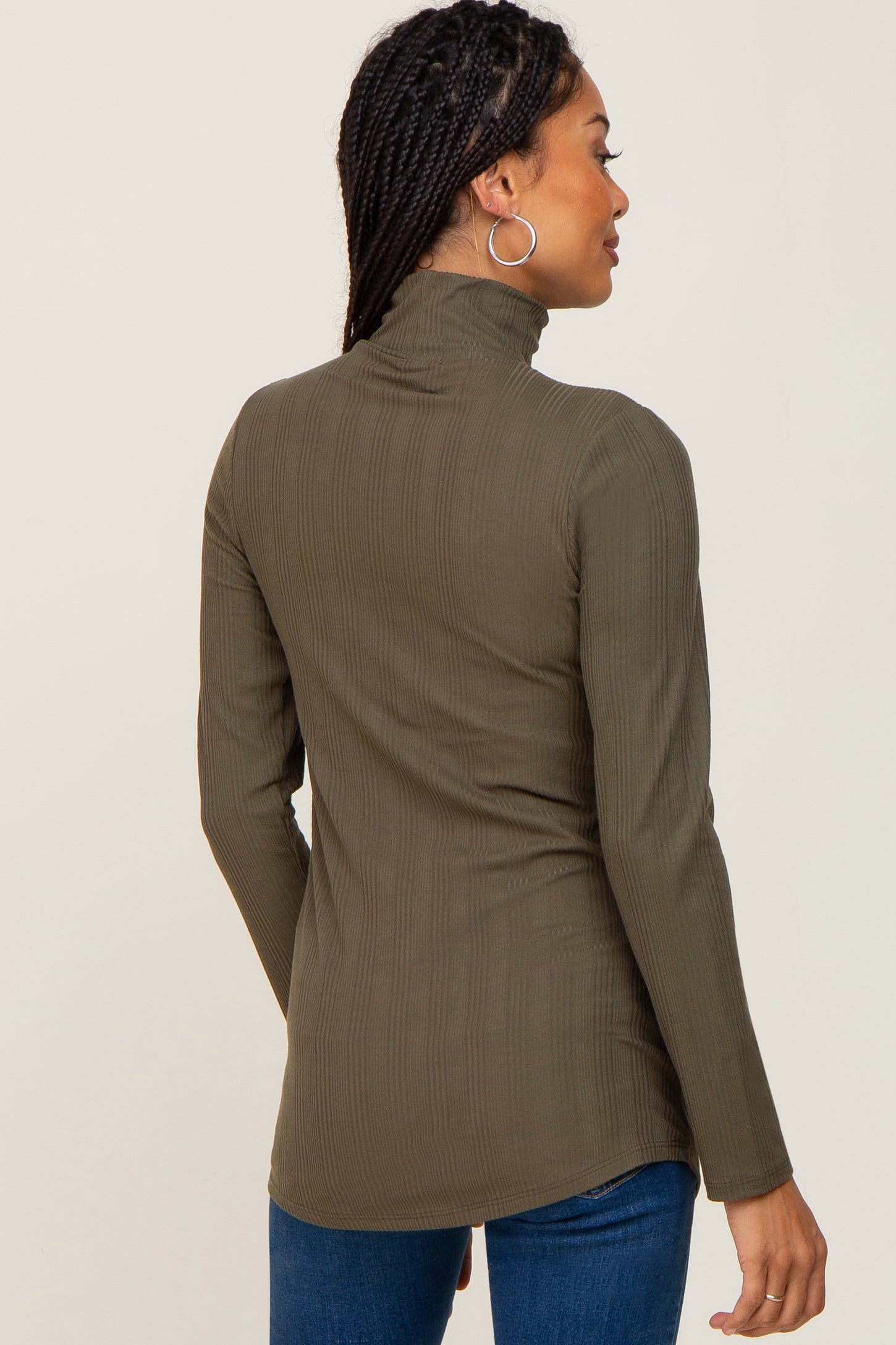 Woman wearing an olive green ribbed turtleneck long sleeve top and blue jeans viewed from the back
