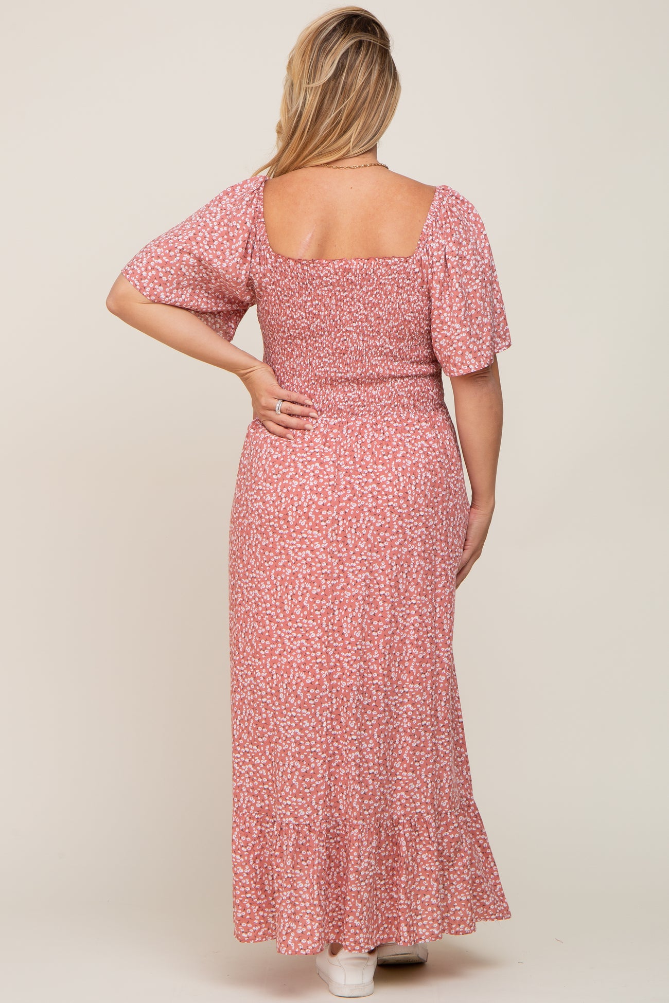 Back view of a woman wearing a pink floral smocked maternity maxi dress with short flutter sleeves