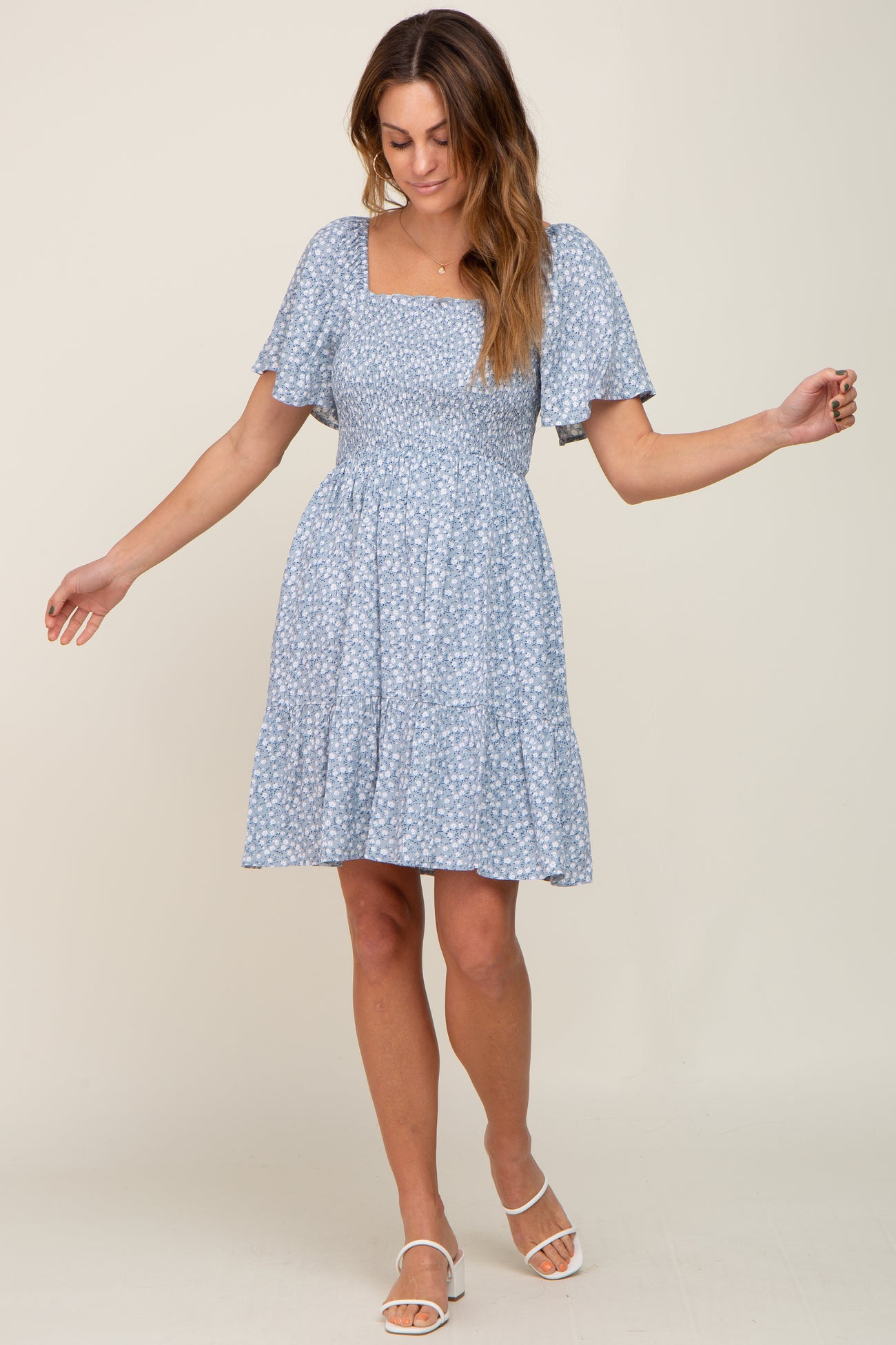 woman wearing a light blue floral smocked maternity dress with flutter sleeves and white sandals