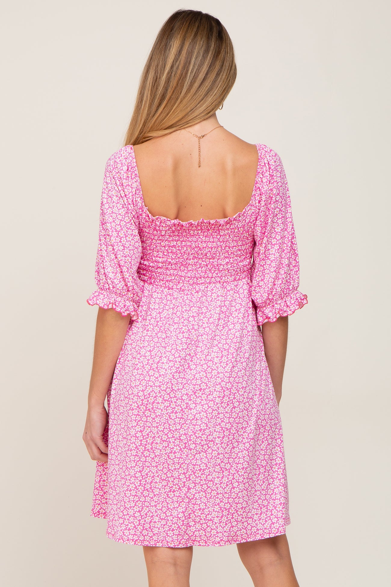 Back view of woman wearing pink floral smocked dress with puff sleeves and square neckline