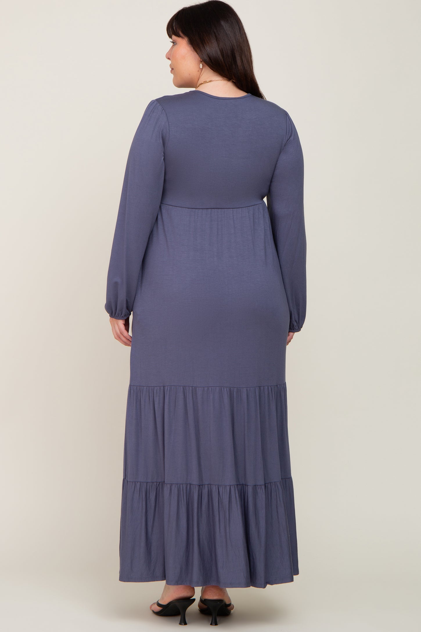 Back view of a woman wearing a long sleeve navy blue tiered maxi dress with a high waist and flowy skirt