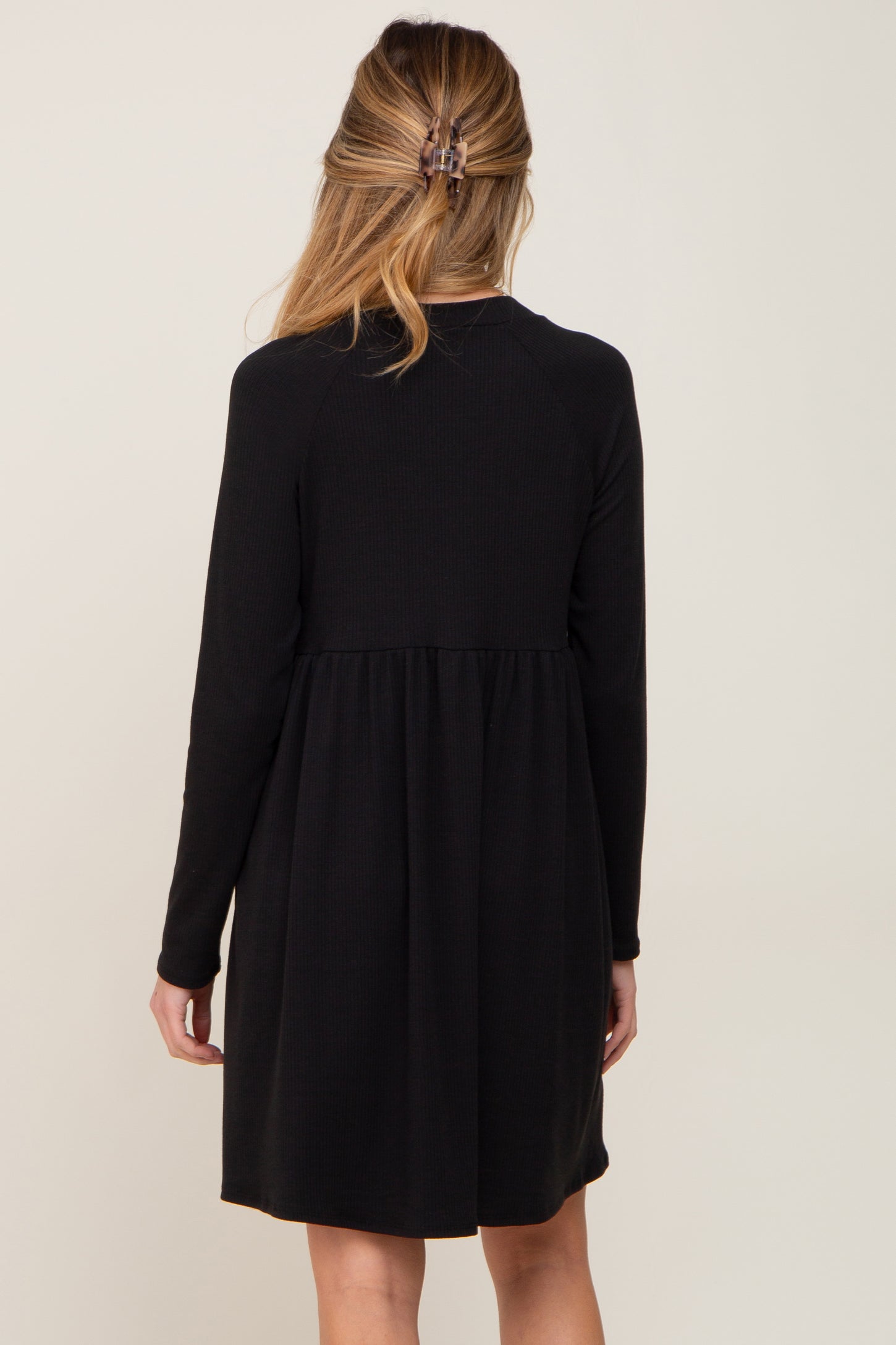 Back view of a woman wearing a long sleeve black ribbed babydoll dress with a gathered waist.