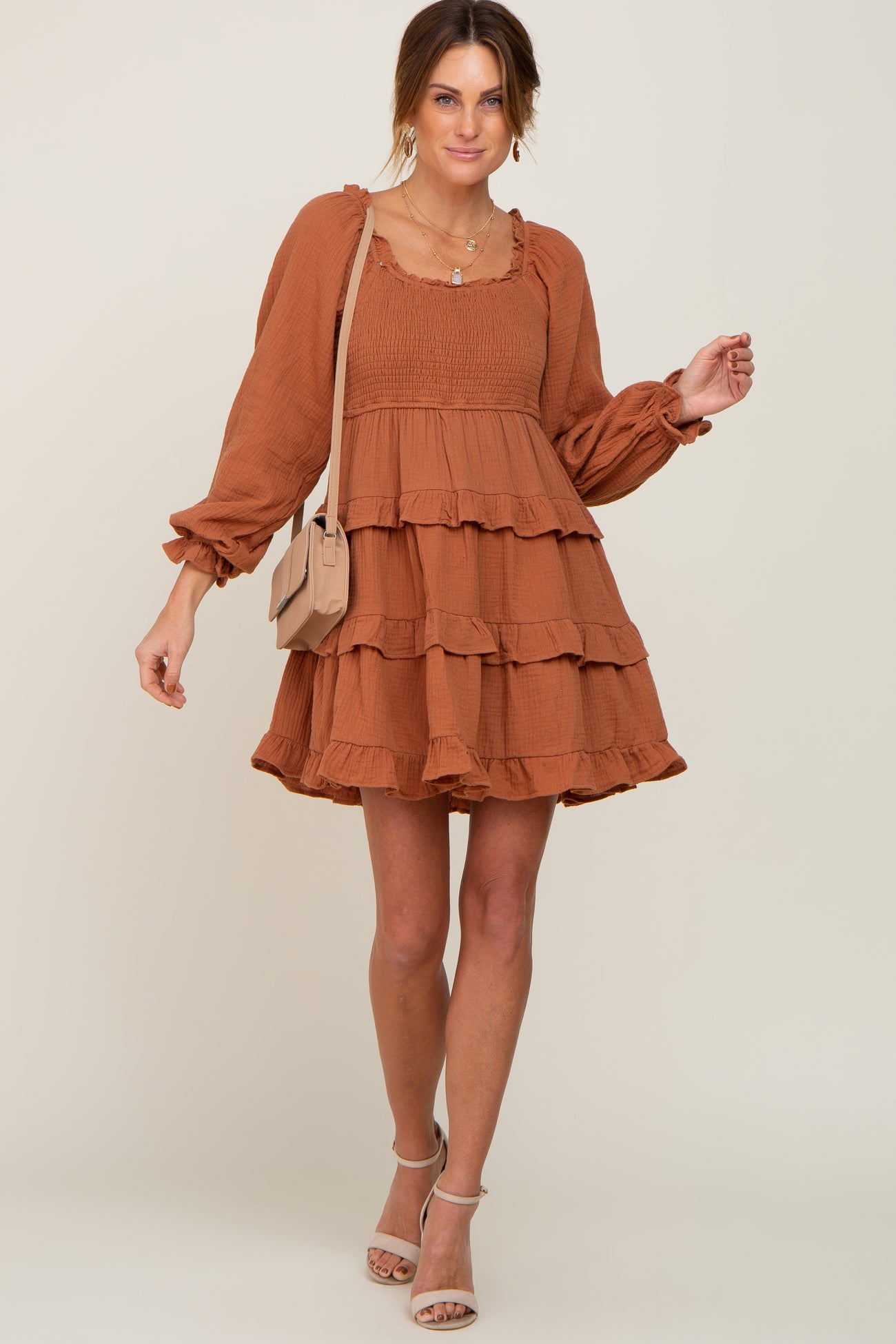 woman wearing a rust orange long sleeve tiered smocked mini dress with a tan crossbody bag