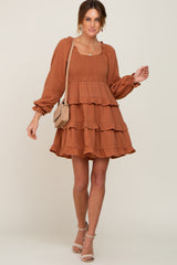 woman wearing a rust orange long sleeve tiered smocked mini dress with a tan crossbody bag