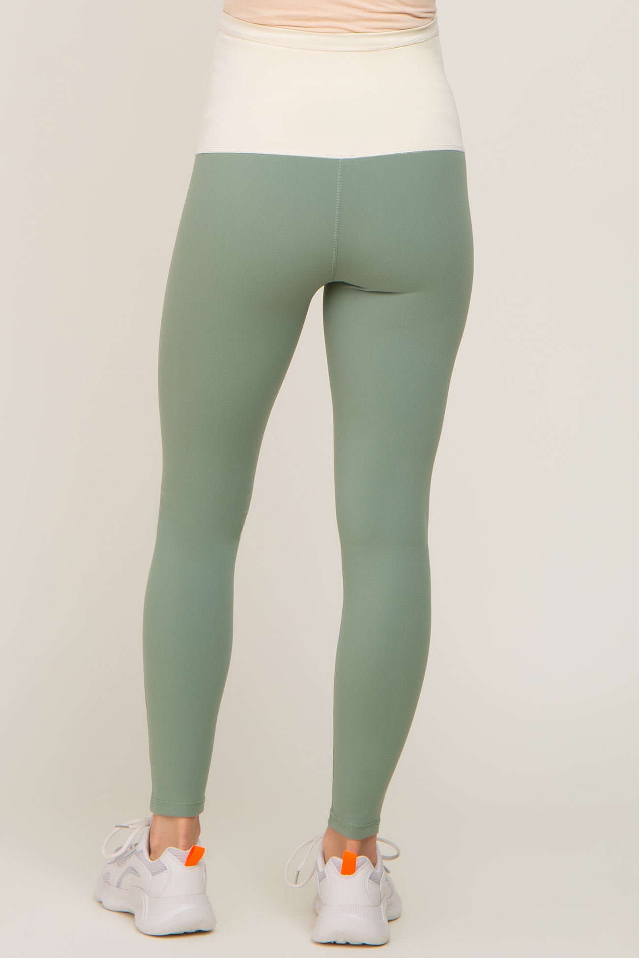 Rear view of person wearing sage green high-waisted leggings and white sneakers against a neutral background