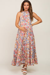 Pregnant woman in a floral halter neck tiered maternity maxi dress with blue and pink flower patterns