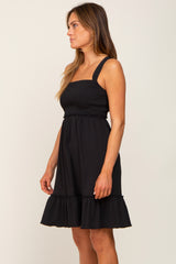 woman wearing a black smocked maternity dress with ruffle hem and square neckline