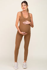 pregnant woman wearing a brown ribbed maternity jumpsuit and white sneakers holding her baby bump