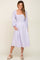 woman wearing a lavender and white plaid smocked midi dress with long sleeves and white wedge sandals