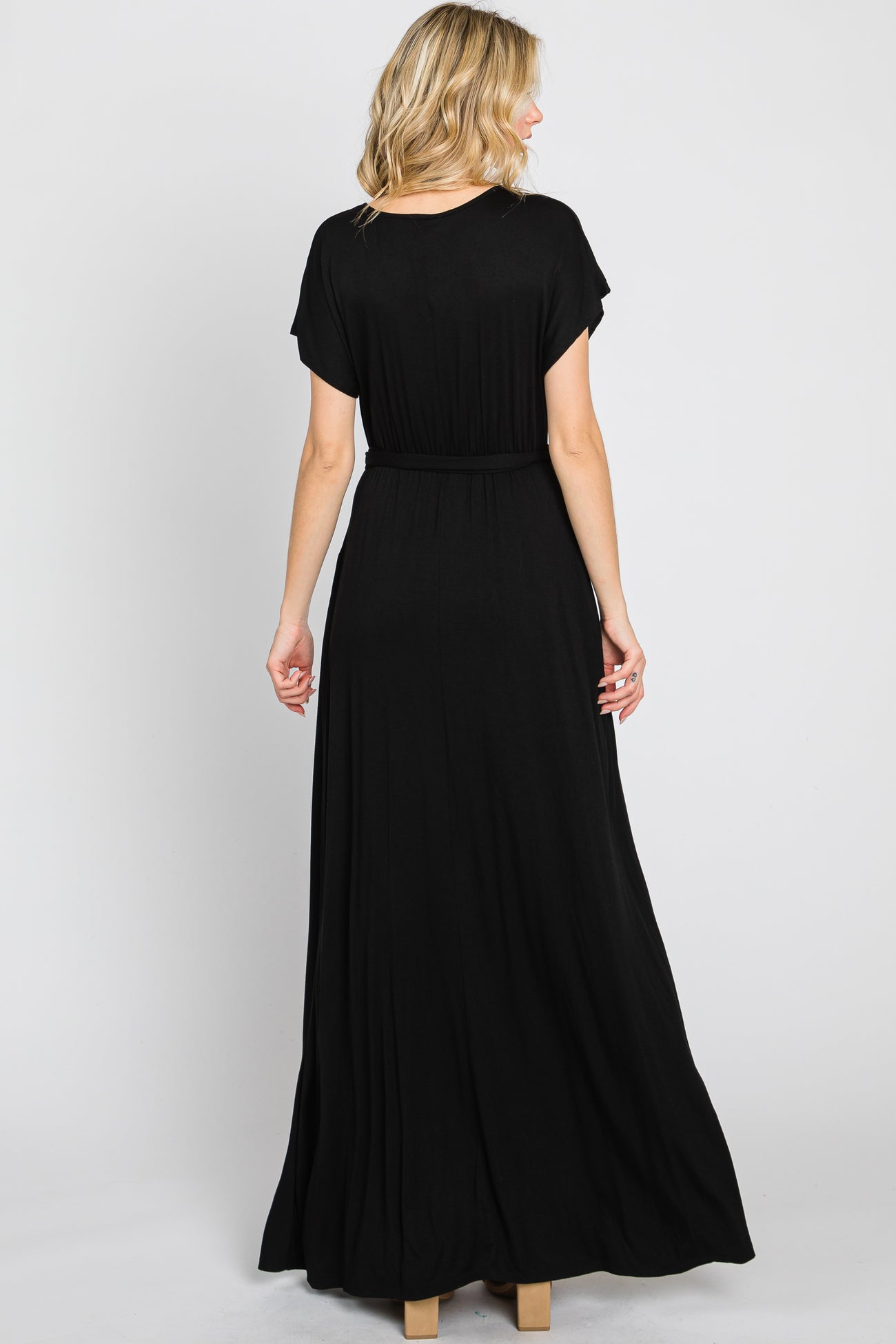Back view of a blonde woman wearing a short sleeve black maxi dress with a cinched waist