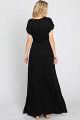 Back view of a blonde woman wearing a short sleeve black maxi dress with a cinched waist