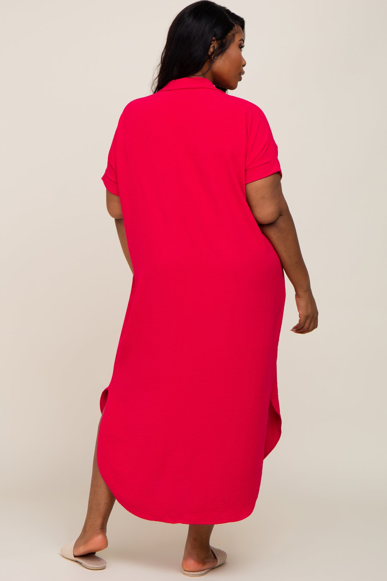 Back view of a woman wearing a plus size hot pink short sleeve midi shirt dress with side slits