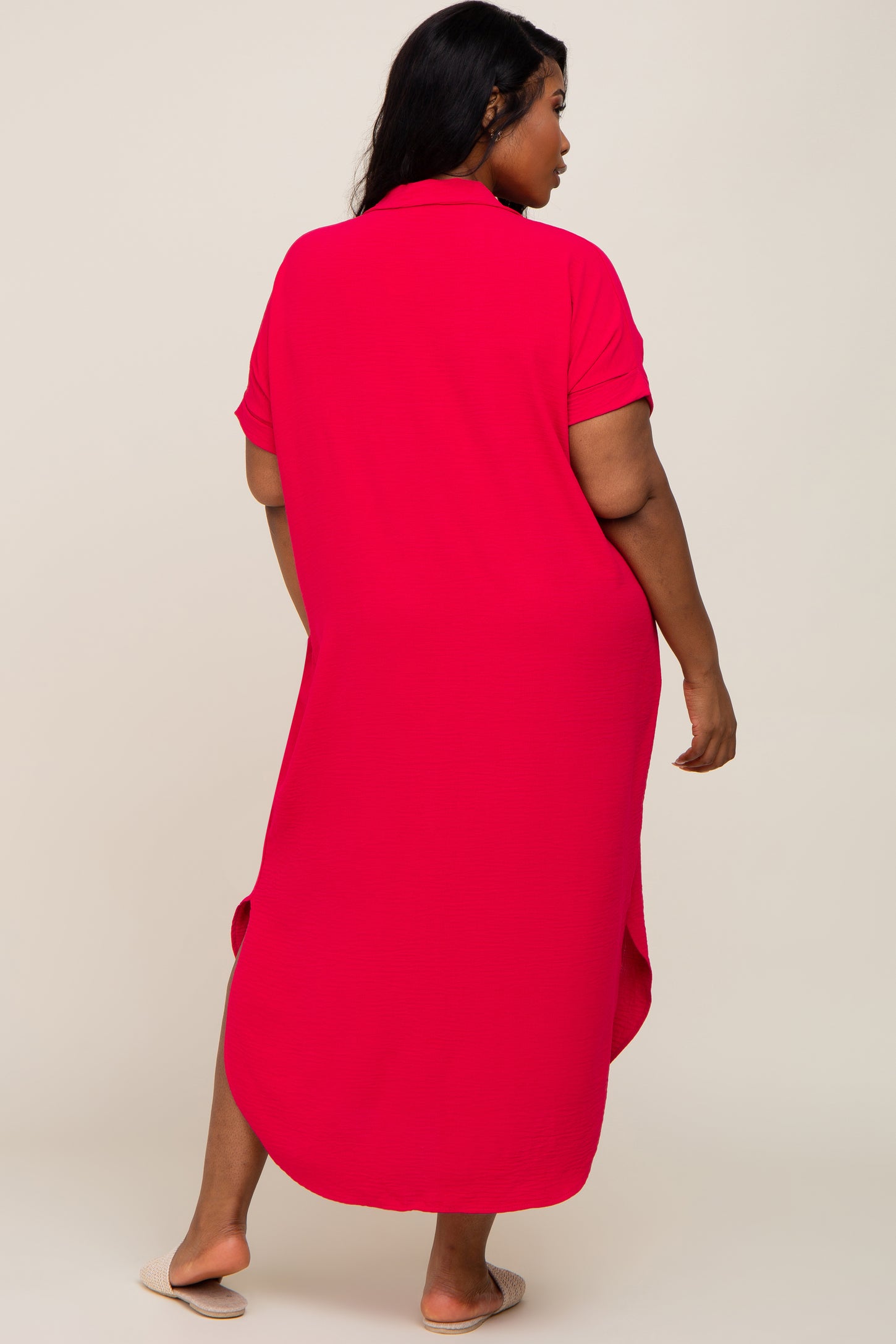 Back view of a woman wearing a plus size hot pink short sleeve midi shirt dress with side slits