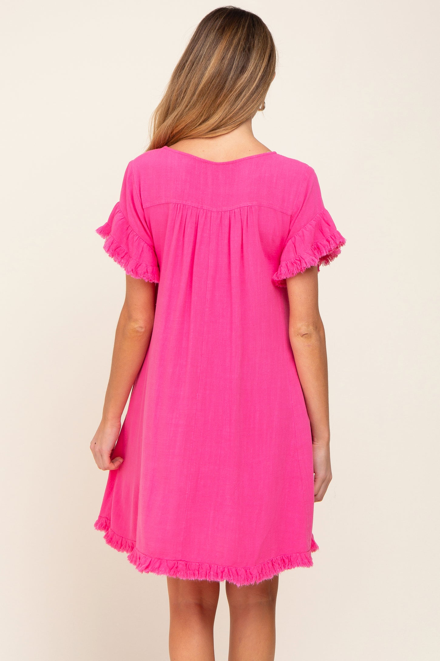 back view of a woman wearing a bright pink short sleeve dress with fringe trim on the sleeves and hem