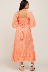 woman wearing an orange floral midi dress with puff sleeves and a tie back waist