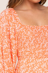 Close up of a woman wearing an orange floral print dress with a smocked bodice and square neckline