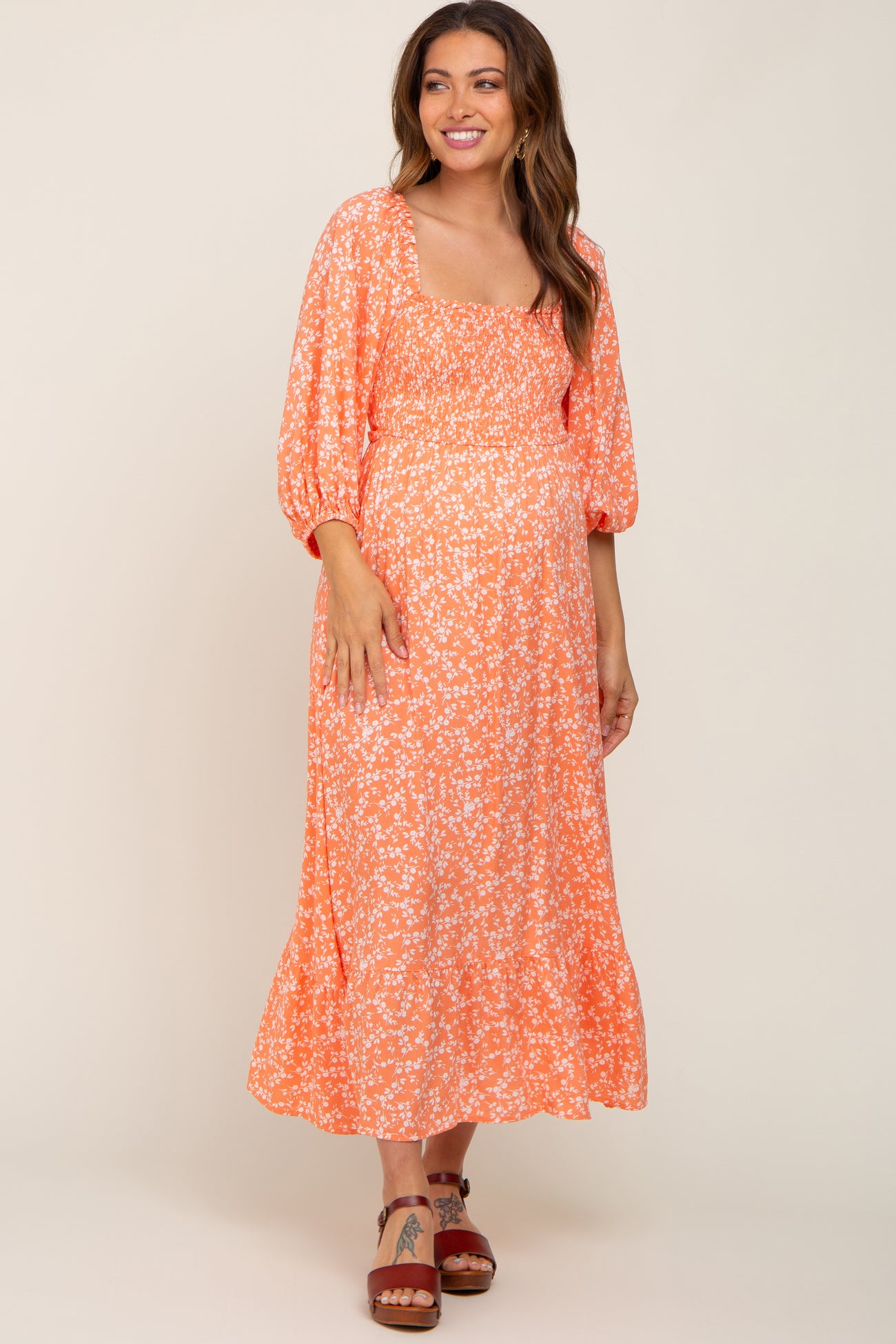 smiling woman wearing orange floral smocked maternity midi dress with puff sleeves