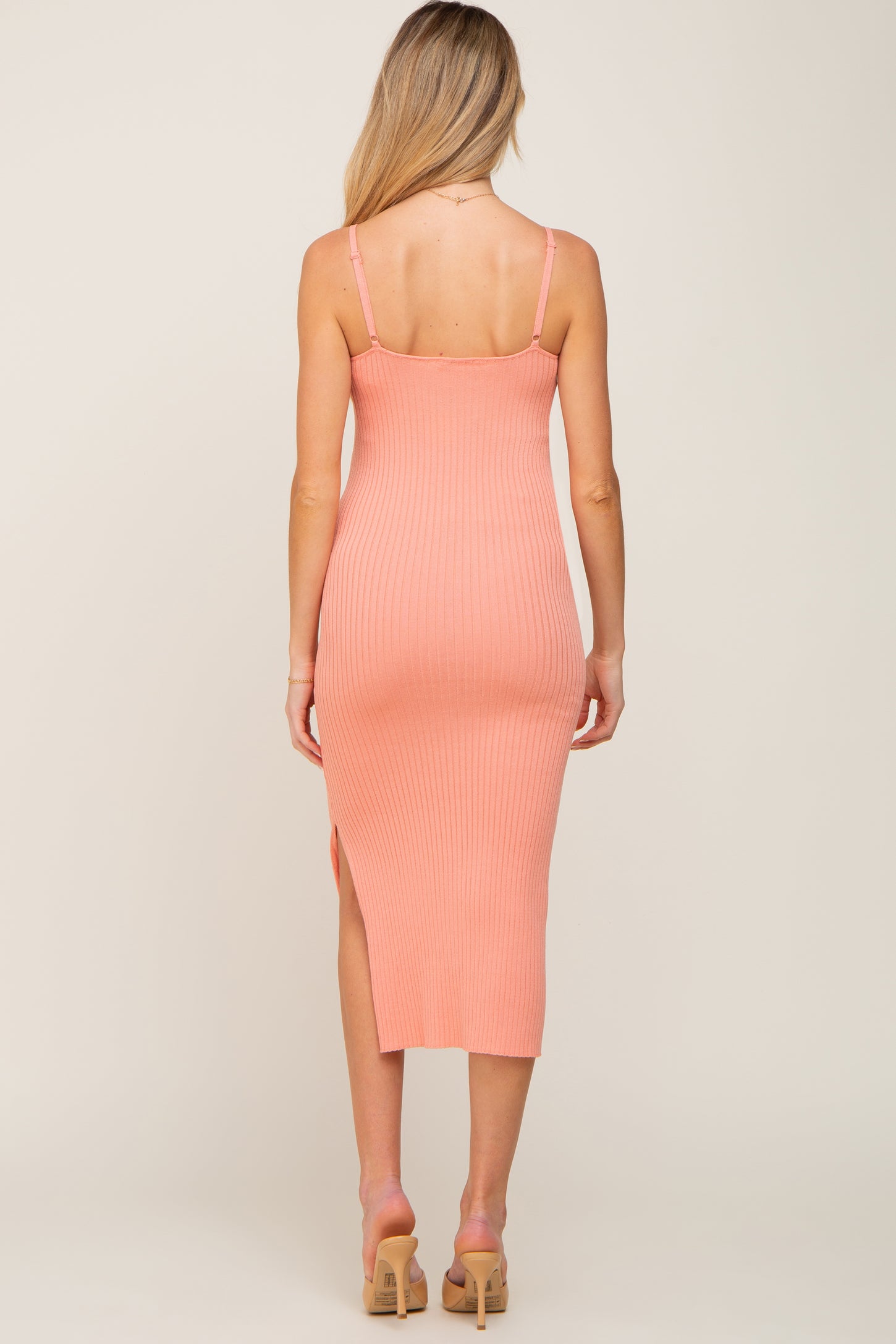 woman wearing a light pink ribbed midi maternity dress with a side slit and adjustable straps, showing her back