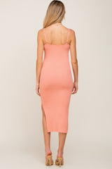 woman wearing a light pink ribbed midi maternity dress with a side slit and adjustable straps, showing her back