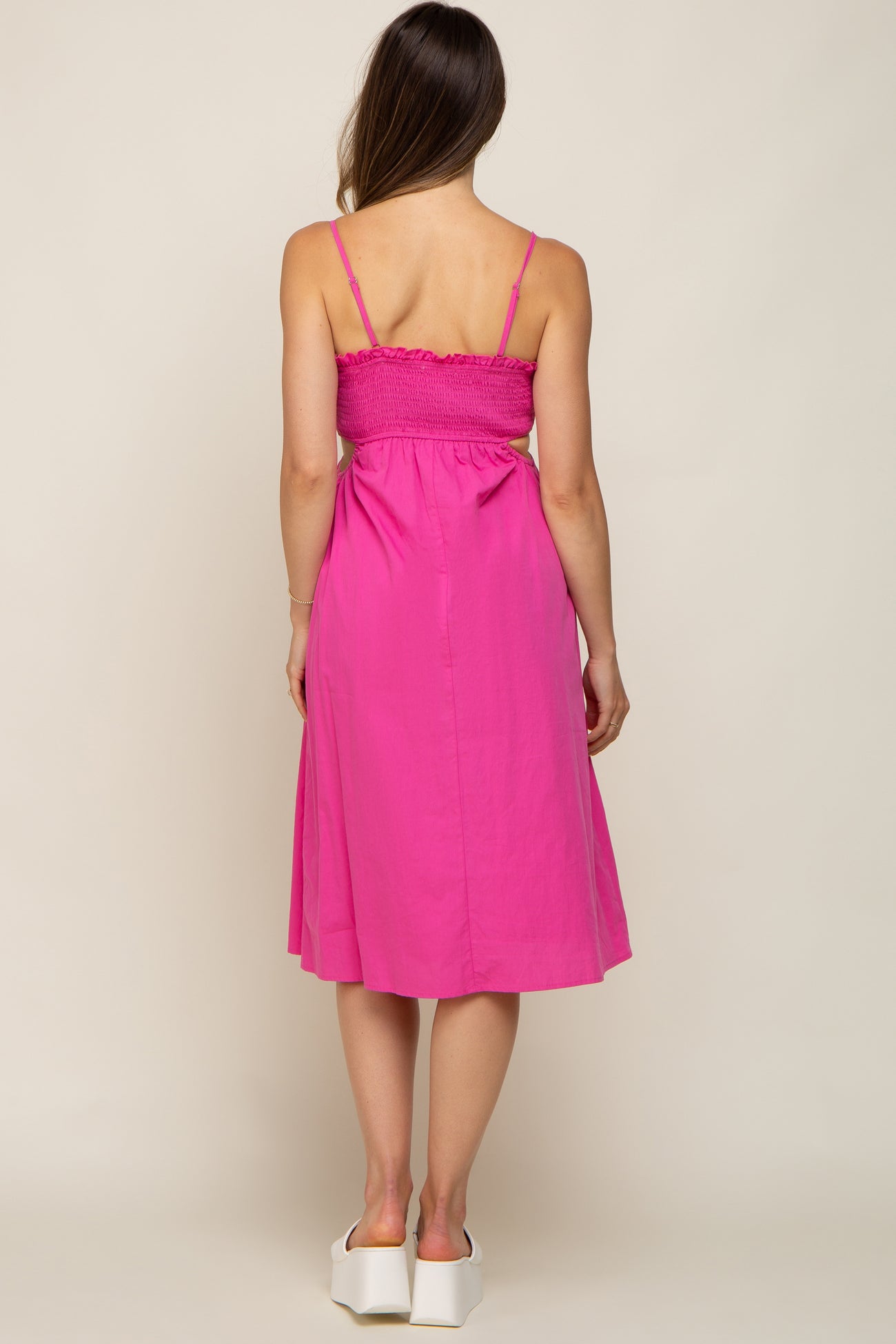Back view of a woman wearing a hot pink midi dress with smocked back and side cutouts