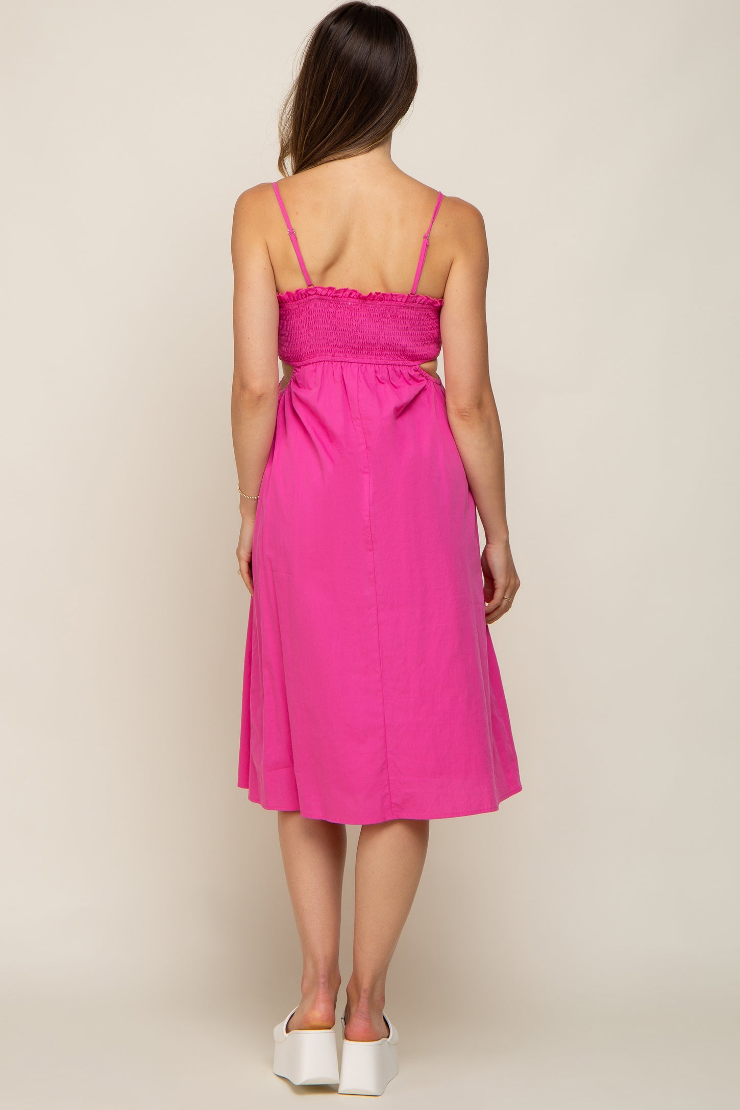 Back view of a woman wearing a hot pink midi dress with smocked back and side cutouts