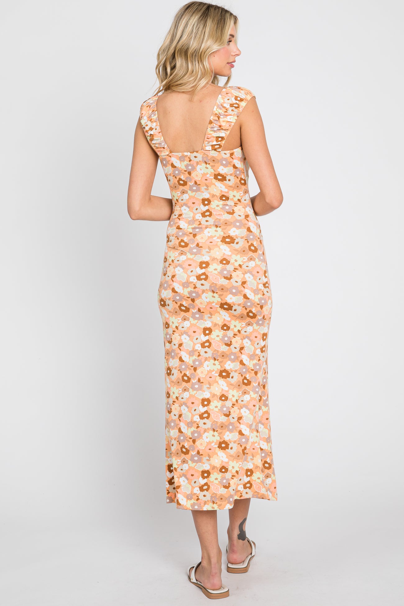 Woman from behind wearing a peach floral midi dress with ruffled straps and white sandals