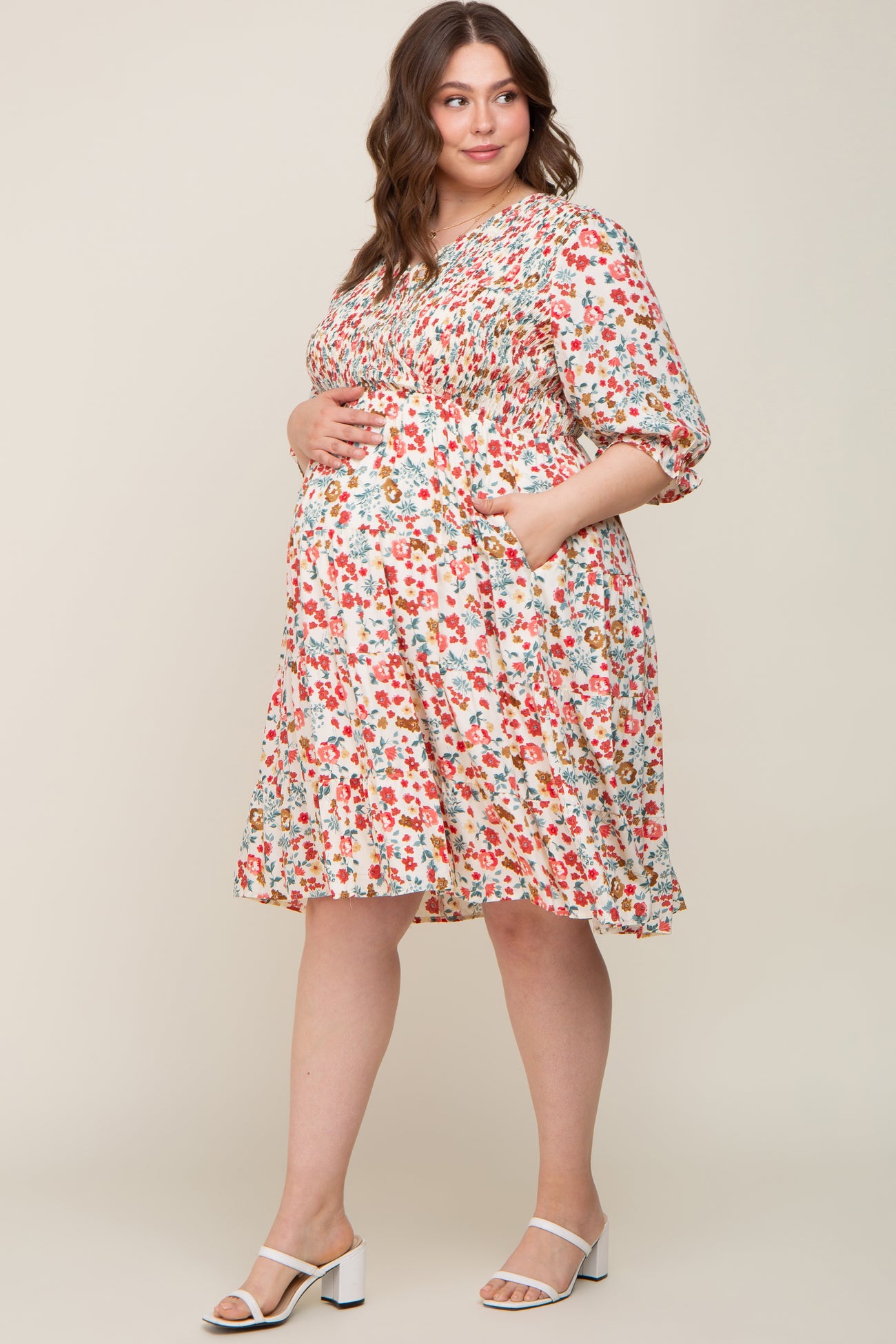 Pregnant woman in a floral smocked maternity dress with pockets and white block heel sandals