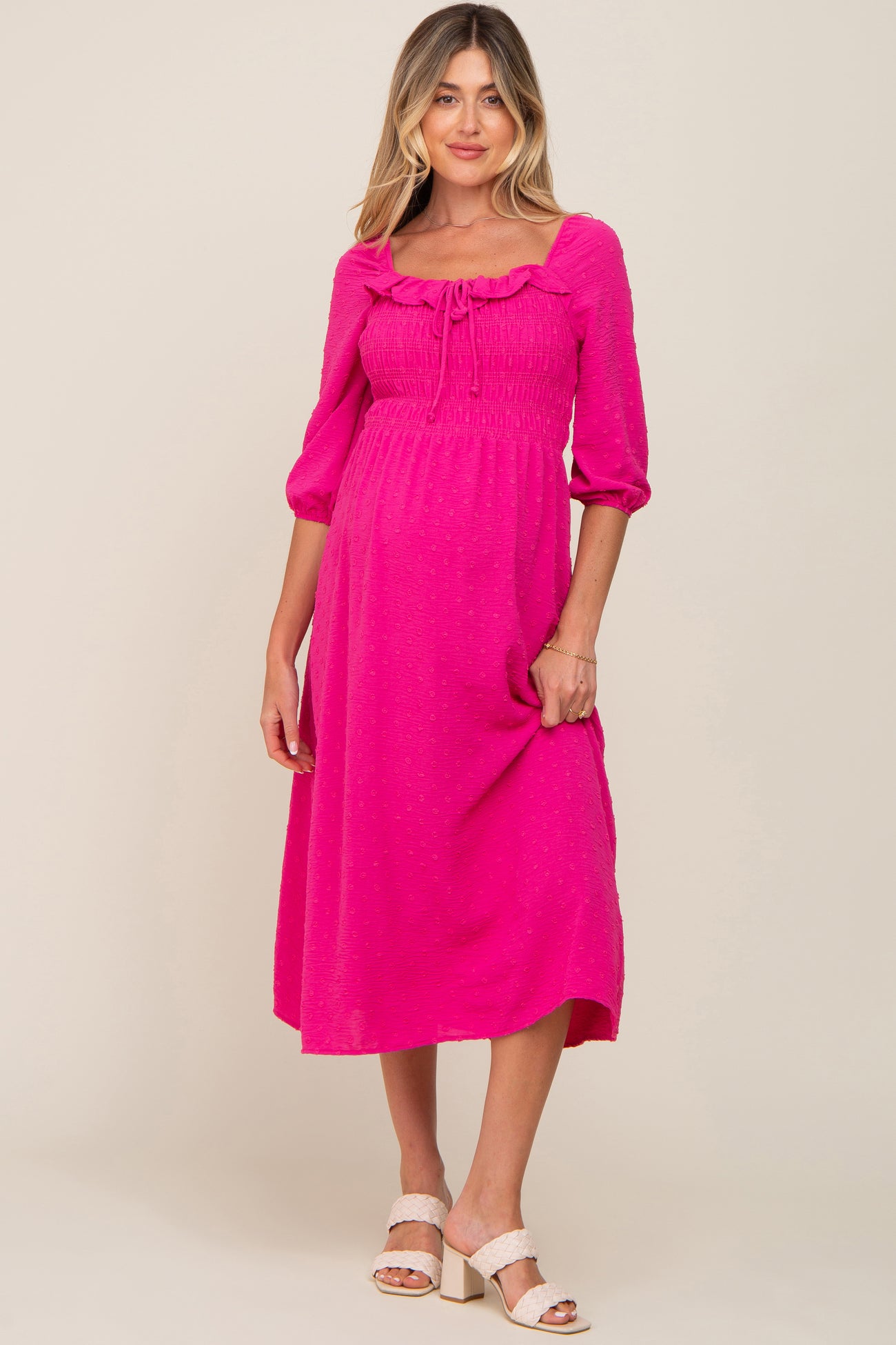 woman wearing a hot pink smocked maternity midi dress with ruffle neckline and three-quarter sleeves
