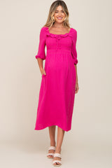 woman wearing a bright pink maternity dress with ruffle details and pockets, showing her baby bump
