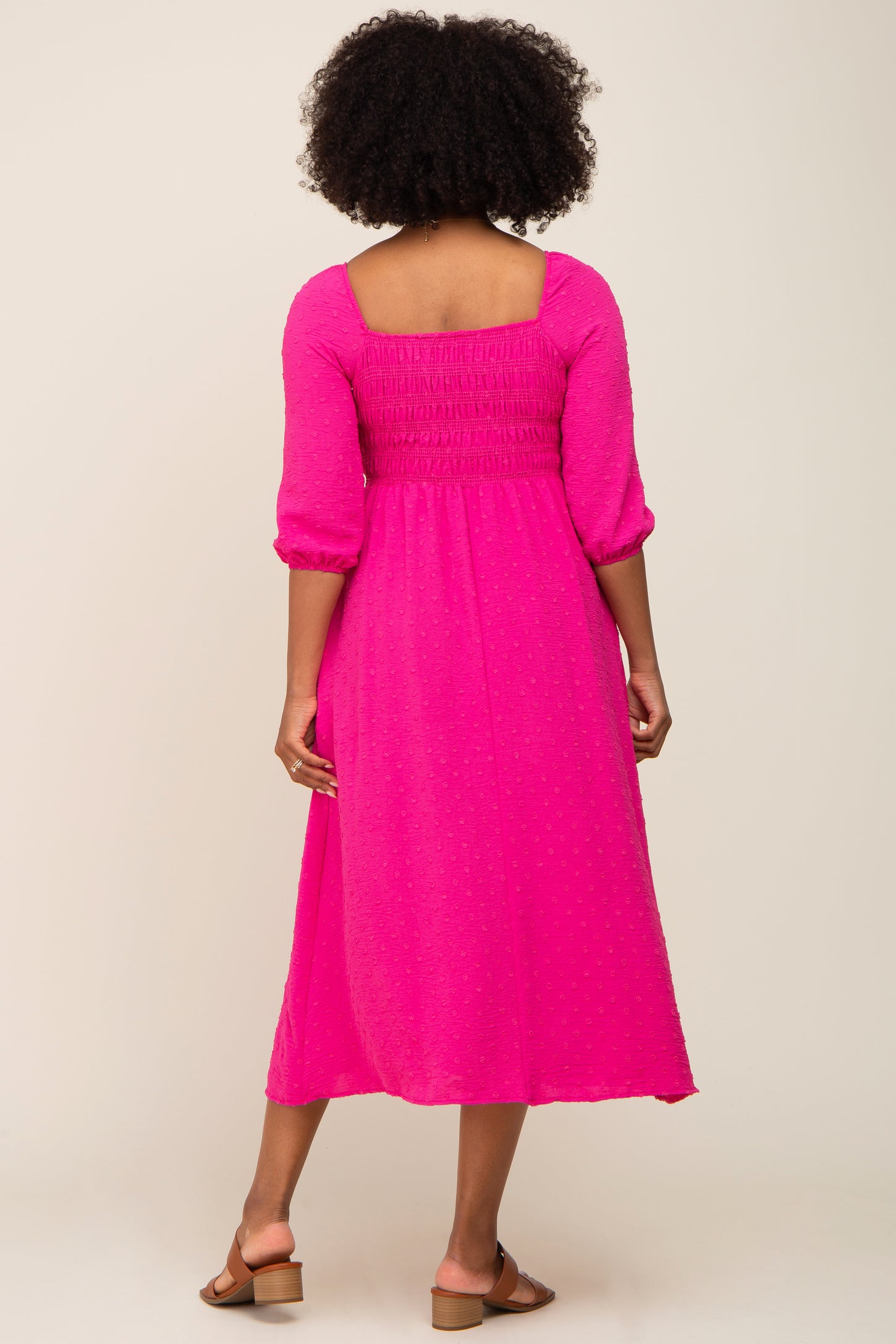 woman wearing a pink midi dress with a square neckline, smocked bodice, and three-quarter puff sleeves, viewed from the back