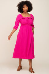woman wearing a bright pink midi dress with puff sleeves and a tie neckline, posing with one hand in pocket