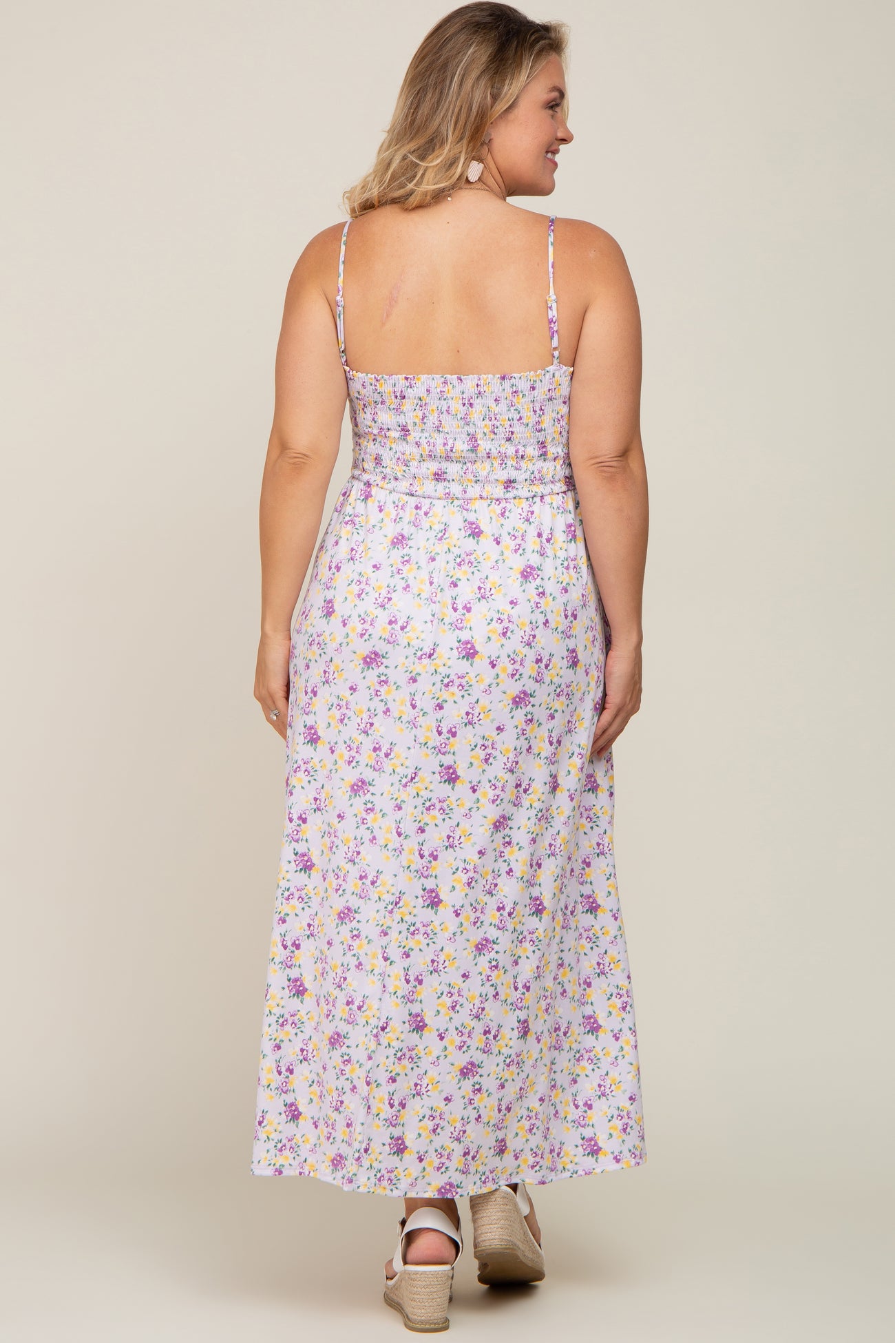 Back view of a woman wearing a purple and yellow floral smocked maxi dress with spaghetti straps and wedge sandals