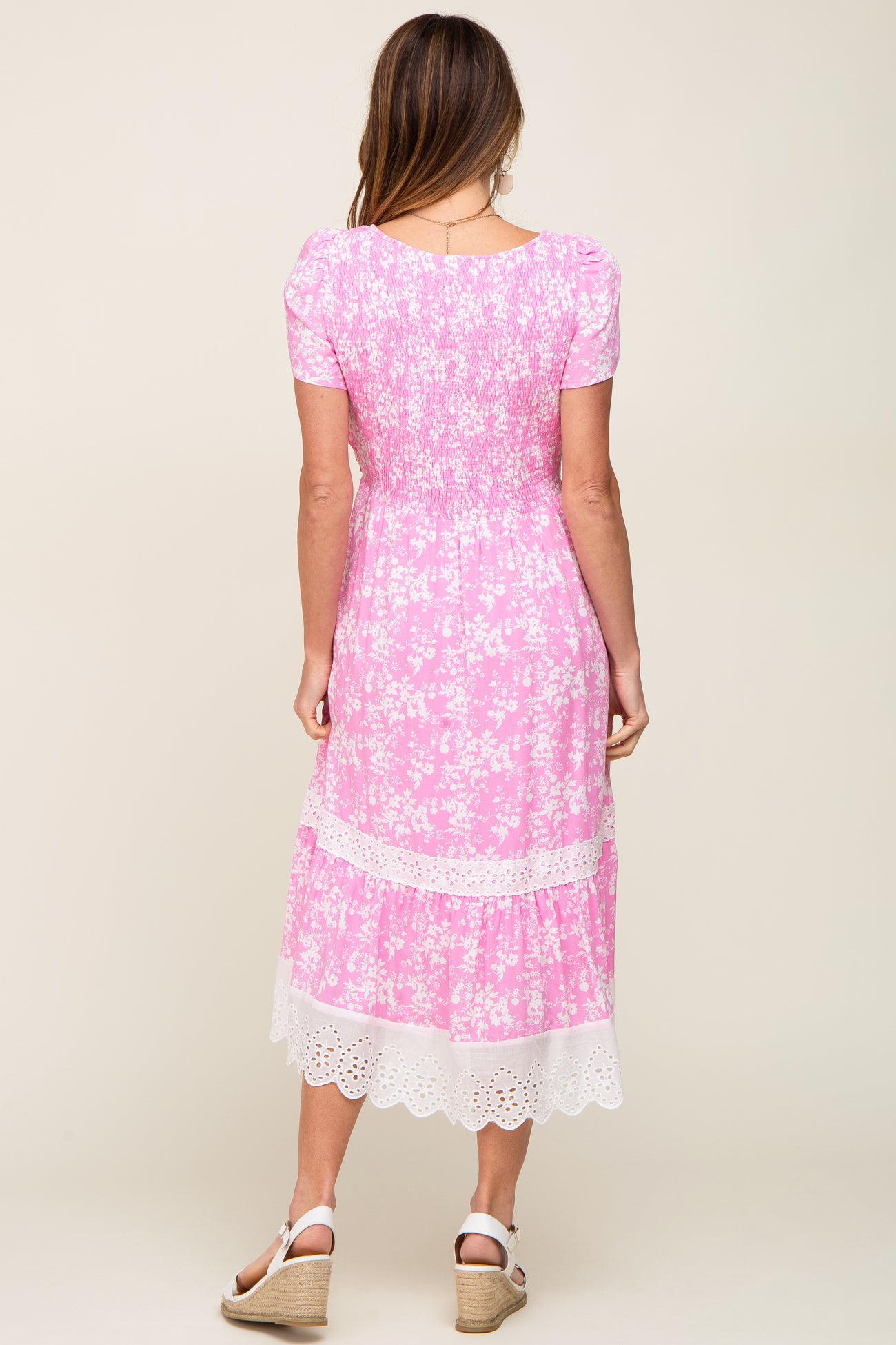 Back view of woman wearing pink floral midi dress with smocked bodice and white eyelet lace trim