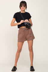 woman wearing black crop top, brown drawstring shorts, and black crossbody bag against a white background