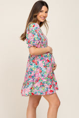 smiling pregnant woman wearing a colorful floral smocked maternity mini dress holding her baby bump