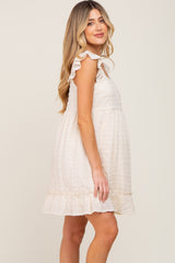 woman modeling a cream sleeveless maternity dress with ruffle straps and a ruffled hem