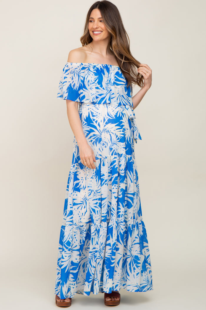 Woman wearing a blue and white tropical palm print off-the-shoulder maternity maxi dress