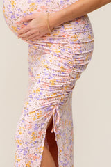 Pregnant woman wearing a pink floral maternity dress with side ruching and a leg slit