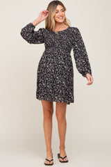 smiling woman wearing a black floral smocked maternity mini dress with long sleeves and black sandals
