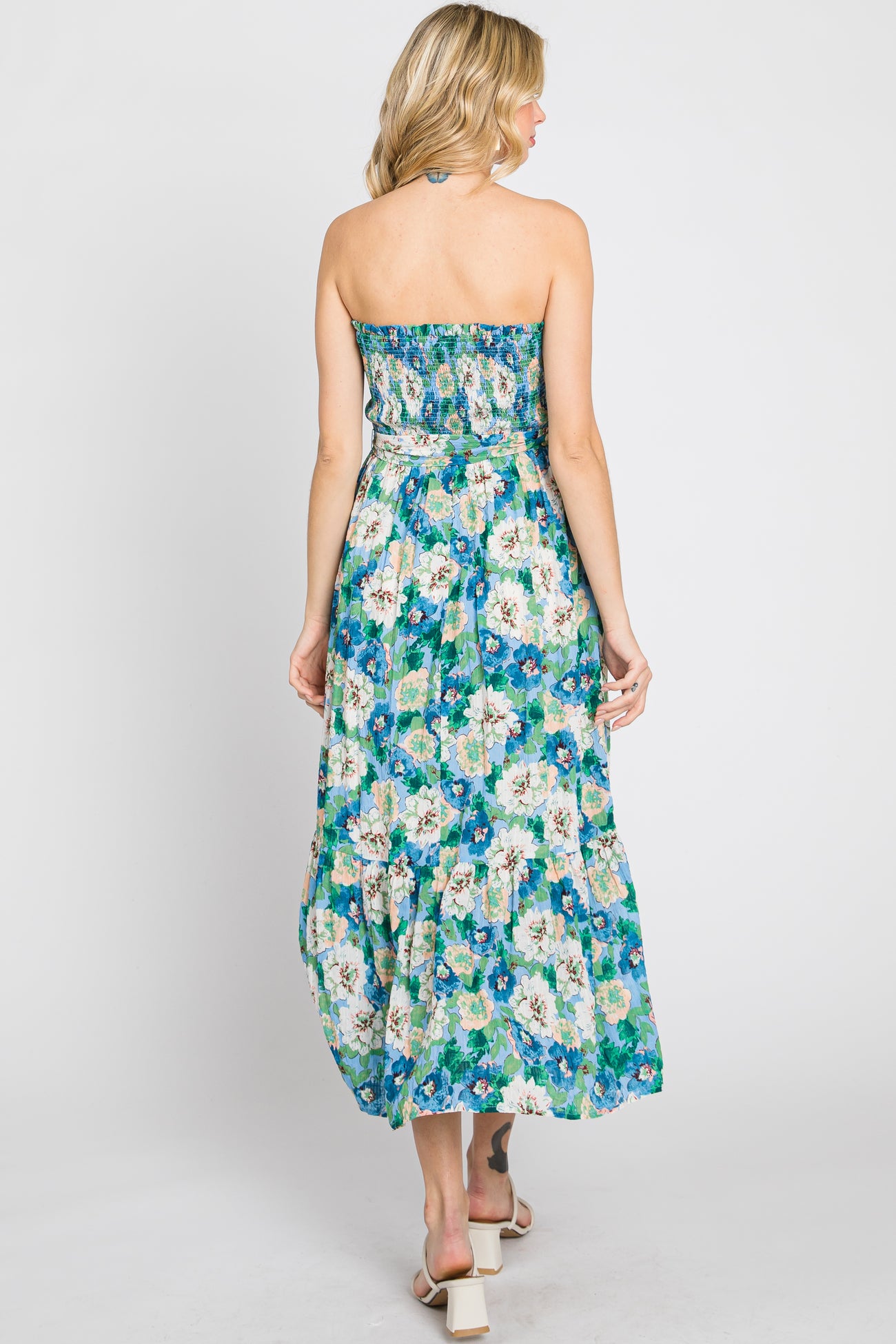 Back view of a woman wearing a strapless blue floral maxi dress with a smocked bodice and tiered skirt
