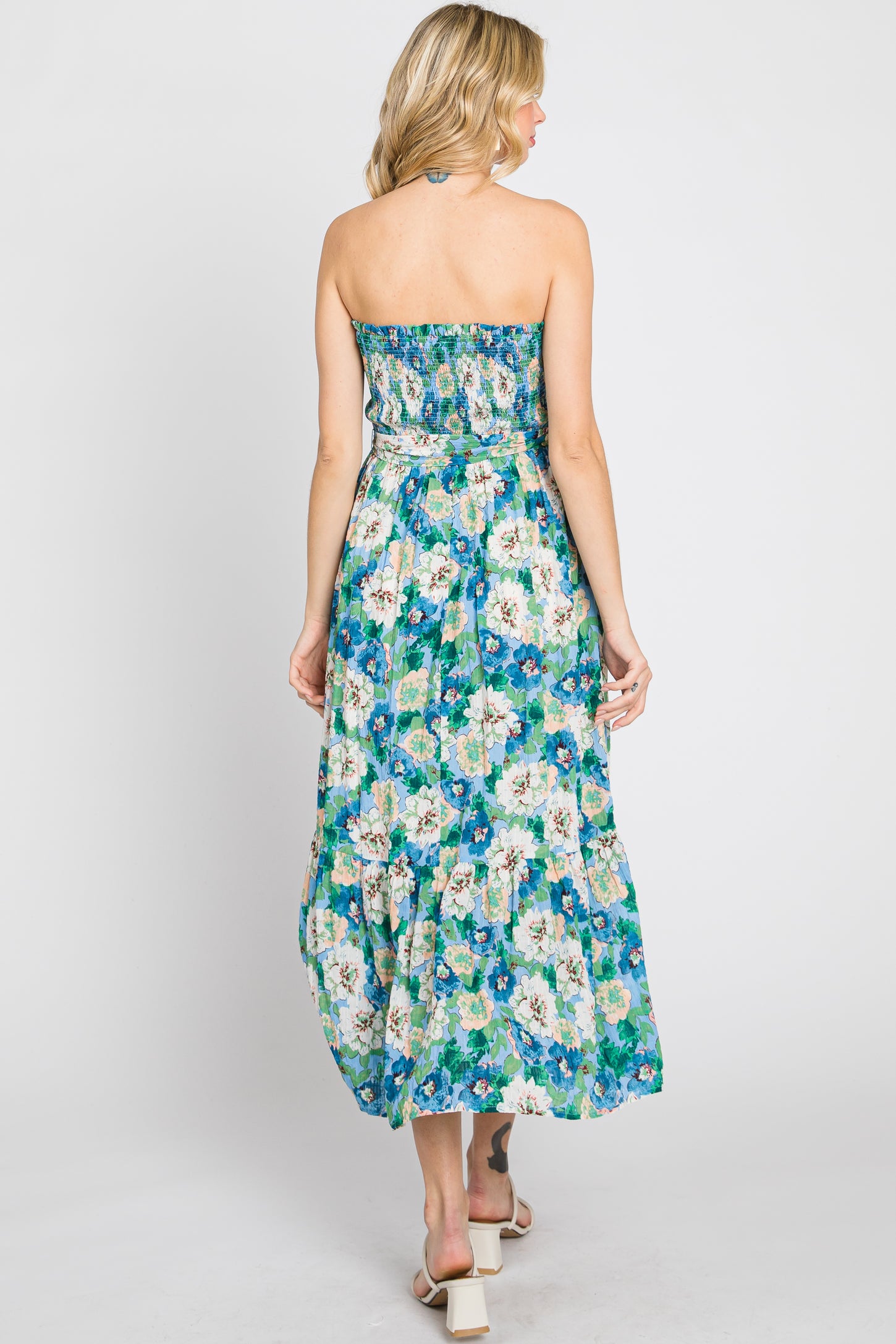 Back view of a woman wearing a strapless blue floral maxi dress with a smocked bodice and tiered skirt