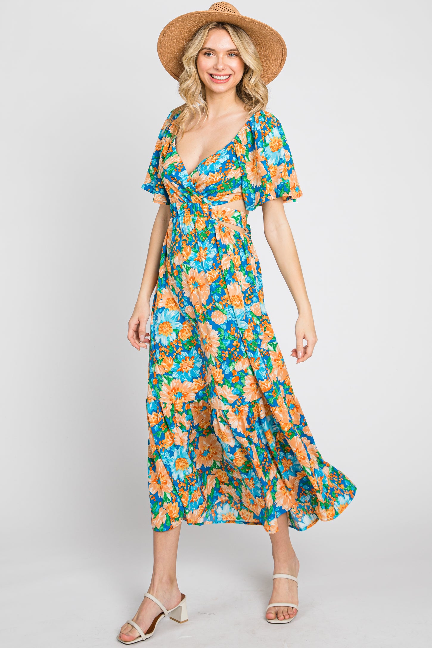 woman wearing a colorful floral wrap dress with short sleeves and a flowing skirt, paired with a straw hat and sandals