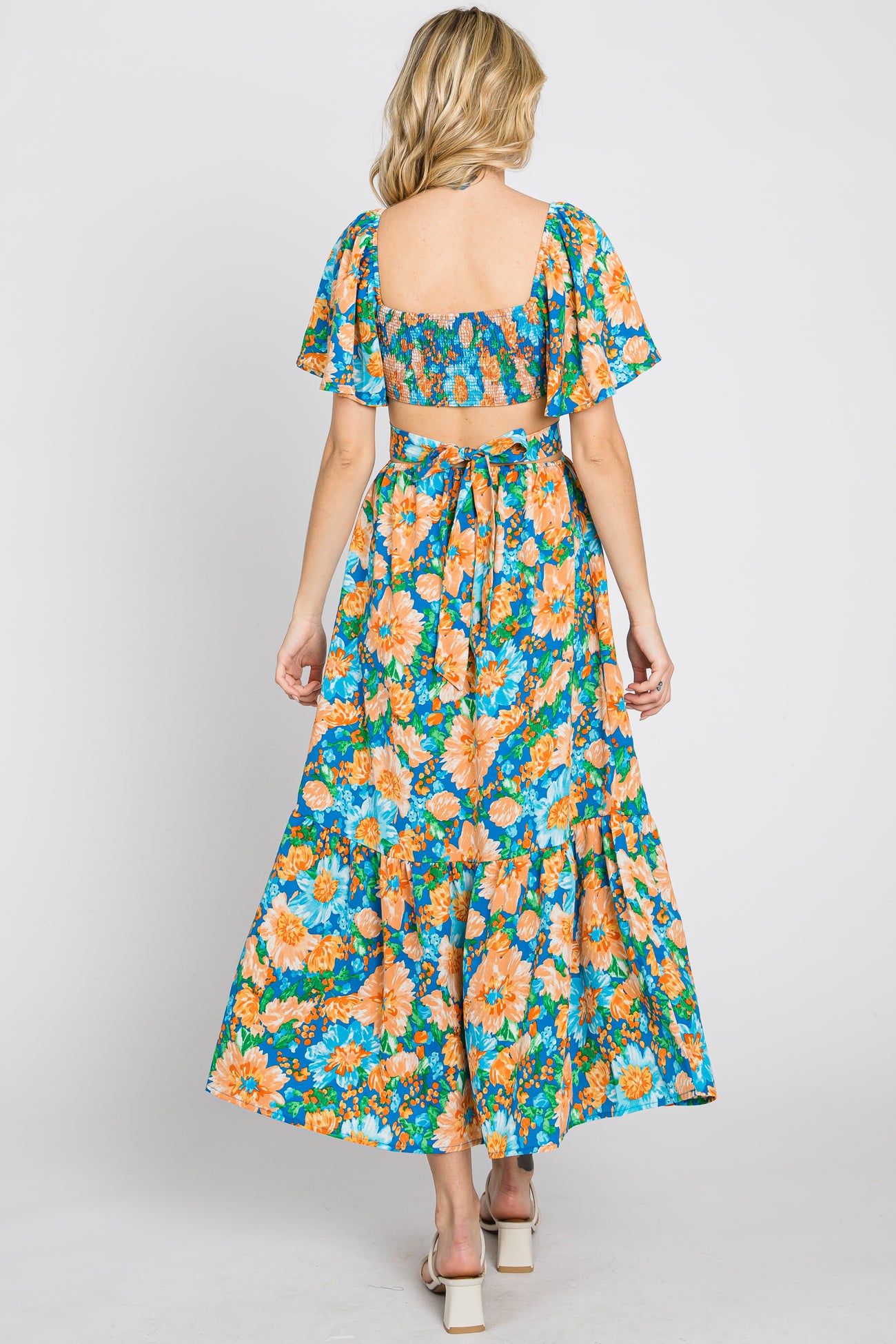 woman wearing a floral maxi dress with short sleeves and an open back, featuring vibrant orange and blue flowers