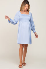 Pregnant woman wearing a light blue smocked maternity dress with long puff sleeves and a square neckline