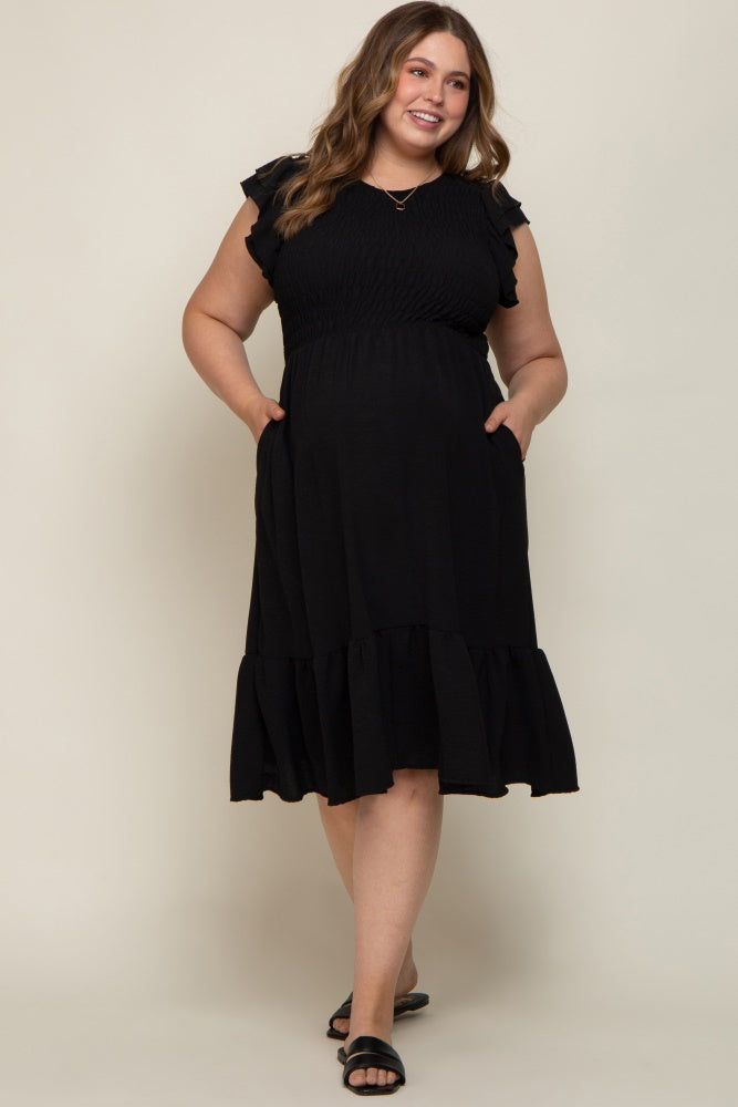 smiling woman wearing a black smocked maternity dress with ruffle sleeves and pockets