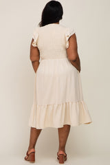 Back view of a woman wearing a cream smocked midi dress with ruffle sleeves and a tiered hem
