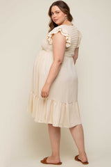 Pregnant woman wearing a cream smocked maternity dress with ruffle sleeves and a tiered hem