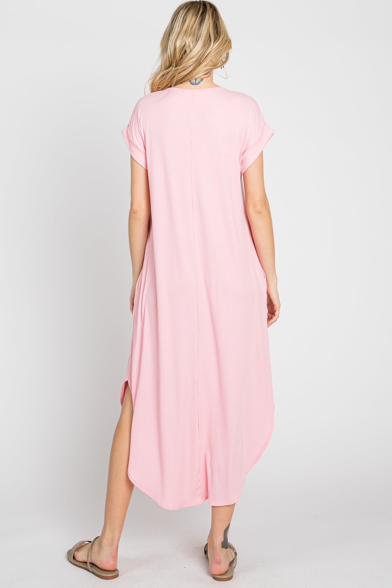 Back view of a woman wearing a light pink short sleeve ribbed midi dress with side slits and a curved hem