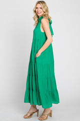 woman wearing a green sleeveless tiered maxi dress with pockets and high ruffle neck